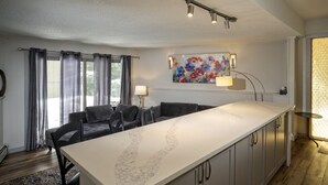 A modern kitchen with a marble countertop, grey cabinets, and a dining area with a sofa and chairs.