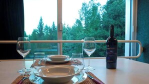 A table set for dining with wine glasses, plates, and cutlery, and a bottle of wine on a table by a window with a view of trees. - Ale 1206 Marilleva 1400, Direct access to slopes  (Marilleva 1400)
