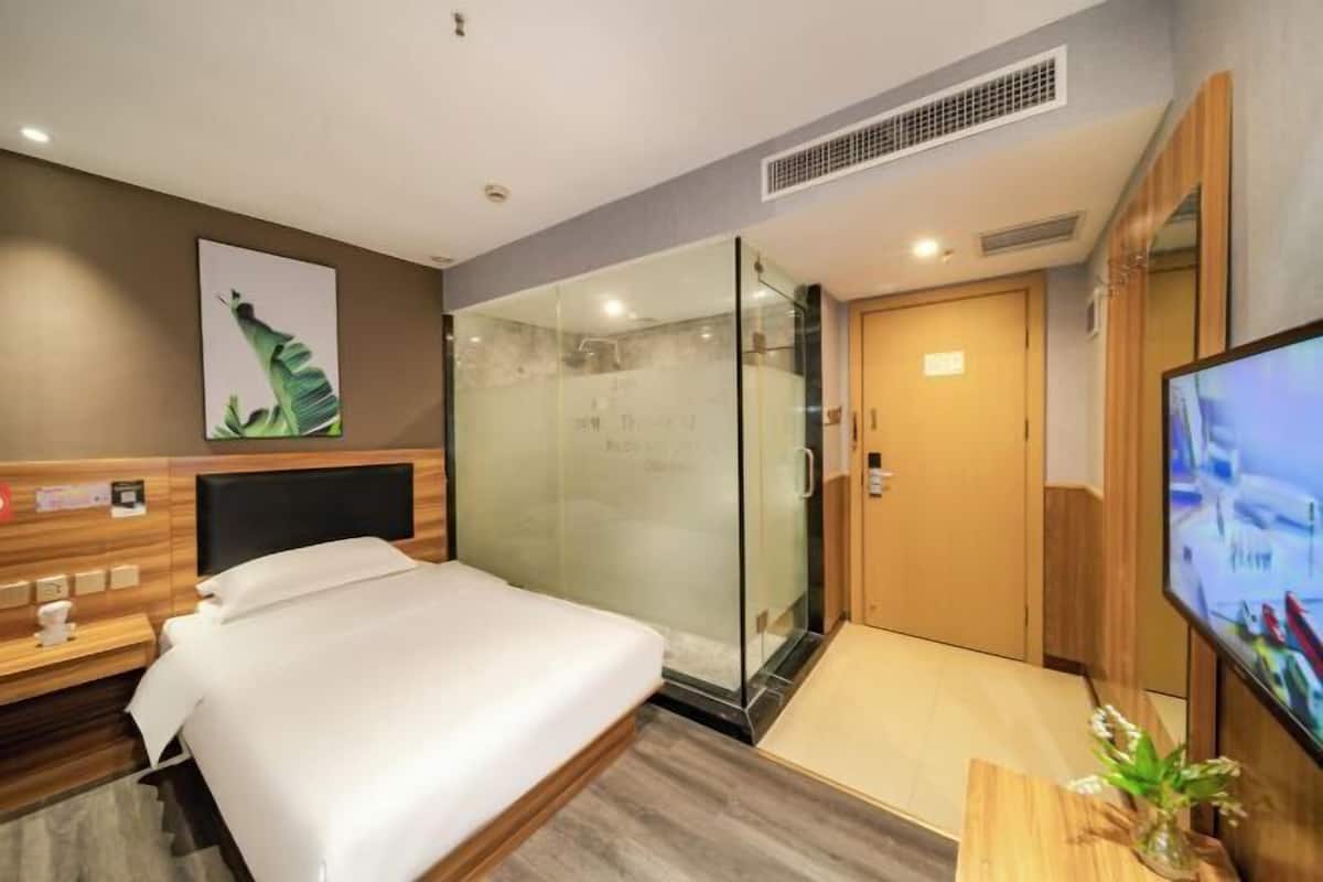 Ein Hotelzimmer mit Bett, Fernseher, Duschkabine aus Glas und Schreibtisch aus Holz.