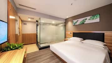 A hotel room with a bed, a desk, a TV, a shower area, and a wall-mounted painting.