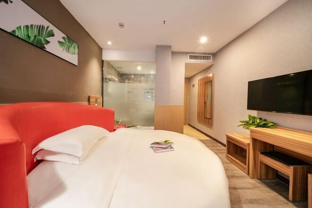 Moderni hotellihuone, jossa on kaareva sänky, televisio, työpöytä ja suihkutila.