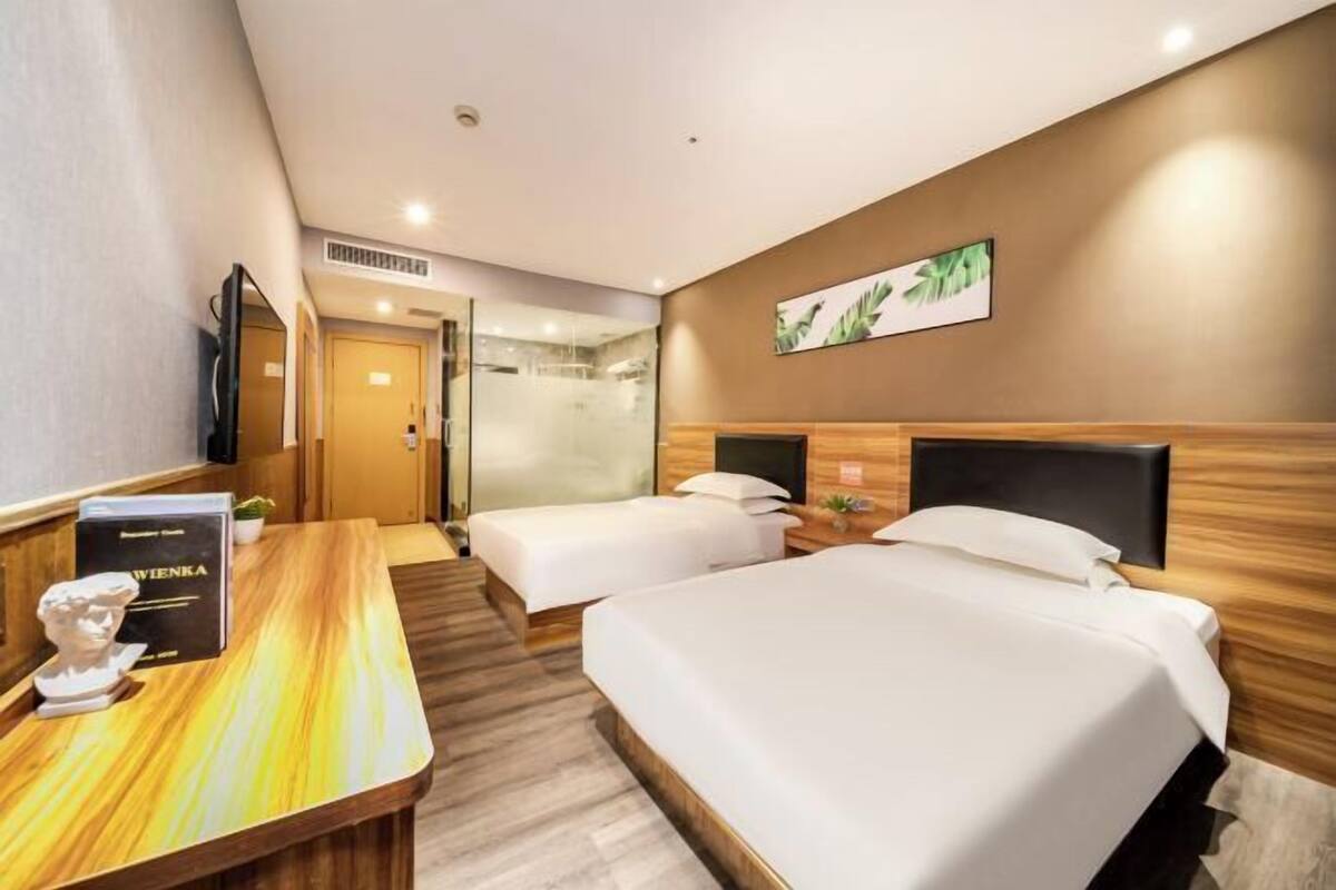 Ein Hotelzimmer mit einem großen Bett, zwei Einzelbetten, einem Schreibtisch mit Stuhl, einem Fernseher und einem Bild an der Wand.