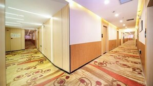 Corredor de hotel com carpete estampado, painéis de madeira e iluminação embutida.