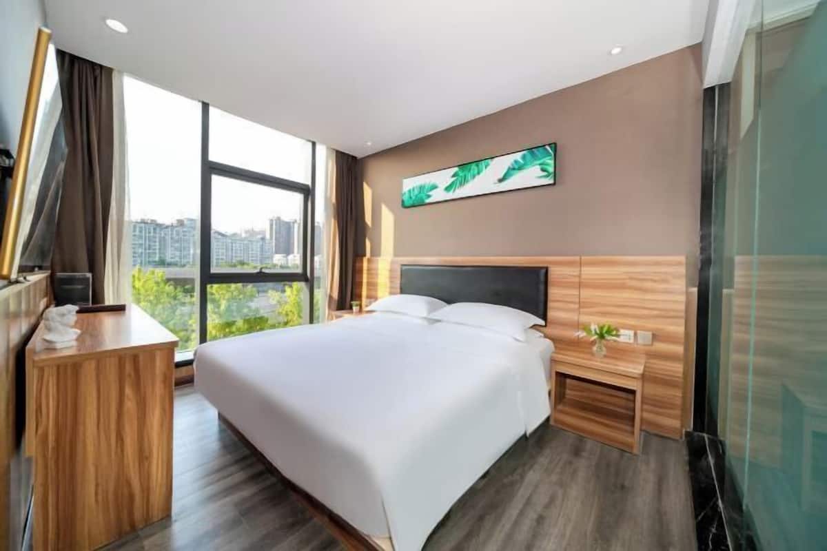 Ein modernes Hotelzimmer mit einem großen Bett, einem Holztisch, einem Nachttisch und Blick auf die Stadt.