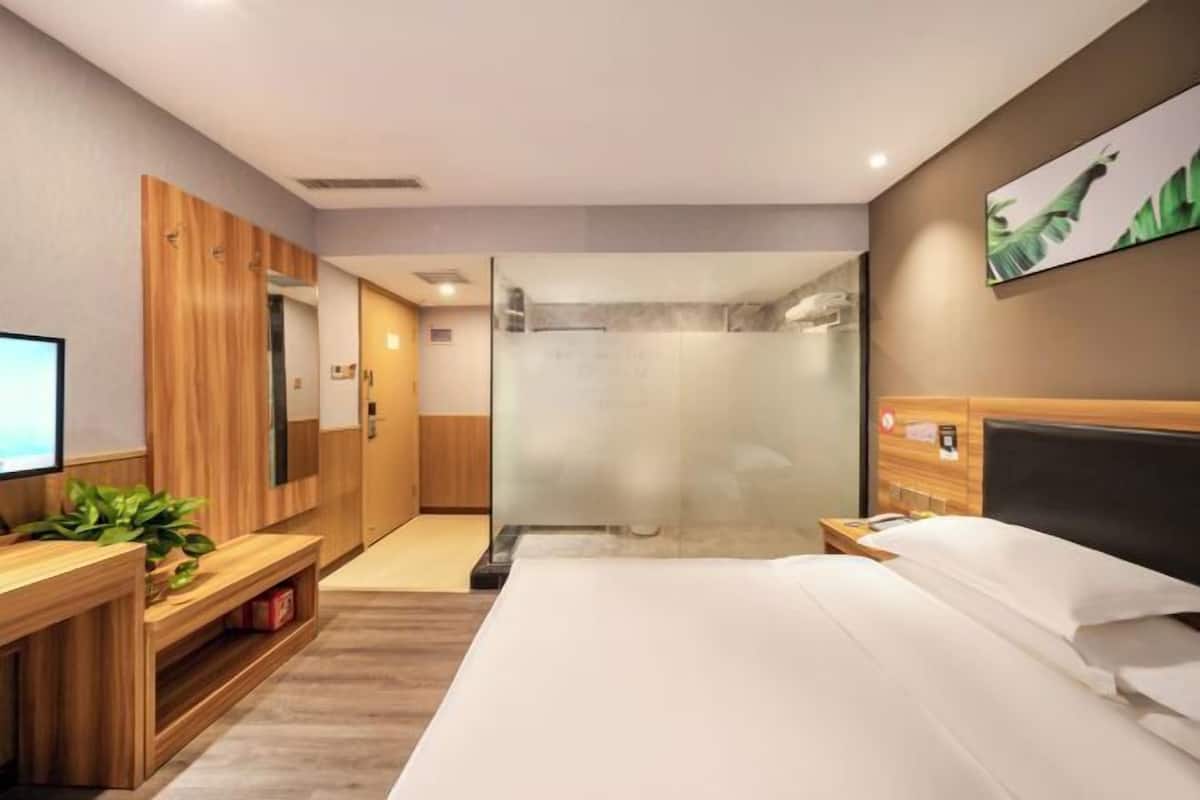 Ein modernes Hotelzimmer mit einem großen Bett, einem Holztisch, einer Duschkabine und einem Fernseher.