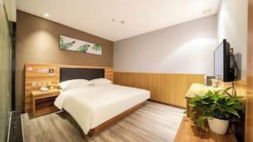 A hotel room with a large bed, wooden headboard, bedside table, and a potted plant.