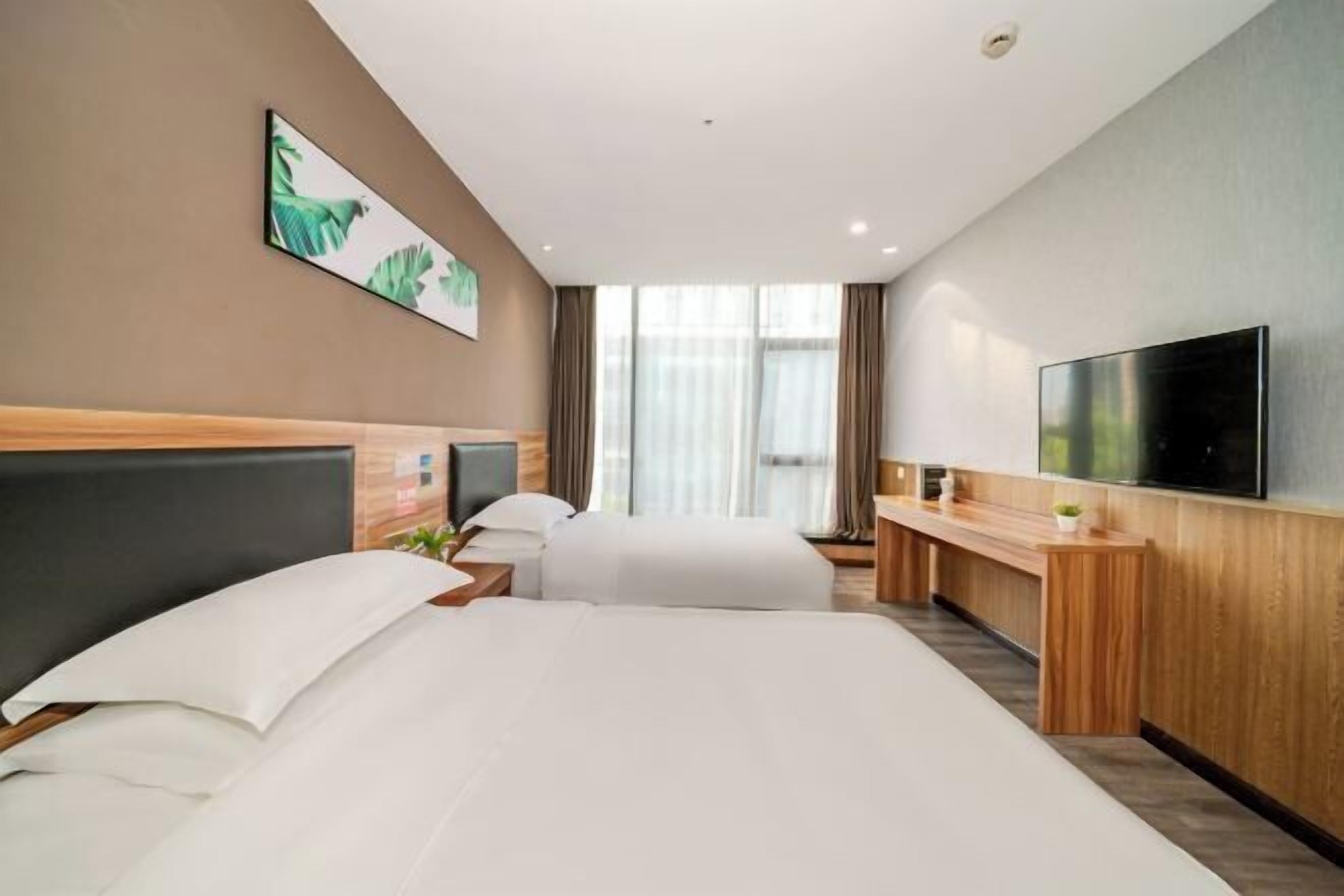 A hotel room with two beds, a desk, a flat-screen TV, and a large window with curtains.