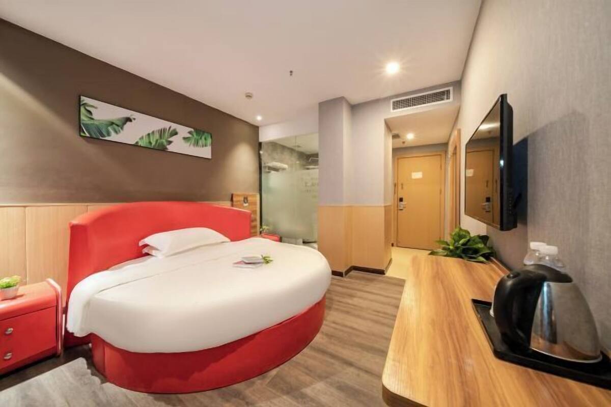Ein modernes Hotelzimmer mit einem gewölbten Bett, einem Holznachtkästchen, einer Kaffeemaschine und einem großen Spiegel.