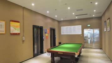 A pool table in a hallway with doors and a bulletin board.