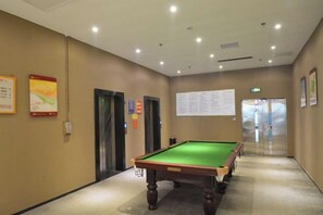 Uma mesa de bilhar em um corredor com portas e um mural de avisos.
