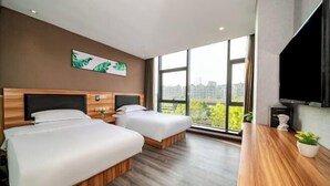 Quarto de hotel com duas camas, uma janela grande com vista para a cidade, televisão de tela plana e escrivaninha de madeira com uma planta.