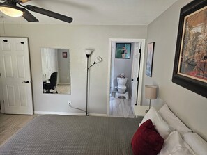 Une chambre à coucher avec un lit, une lampe sur pied, un ventilateur de plafond, une porte et un miroir.