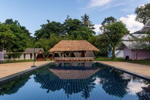 A swimming pool with a thatched-roof structure in the center, surrounded by trees and a building. - Slumber Resort Koh Chang (Ko Chang)