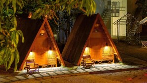 Two wooden A-frame cabins with interior lighting, a stone pathway, and a staircase leading to a building in the background. - Slumber Resort Koh Chang (Ko Chang)