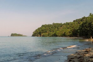 A beach with calm water, a sandy shore, and a forested hill in the background. - Slumber Resort Koh Chang (Ko Chang)
