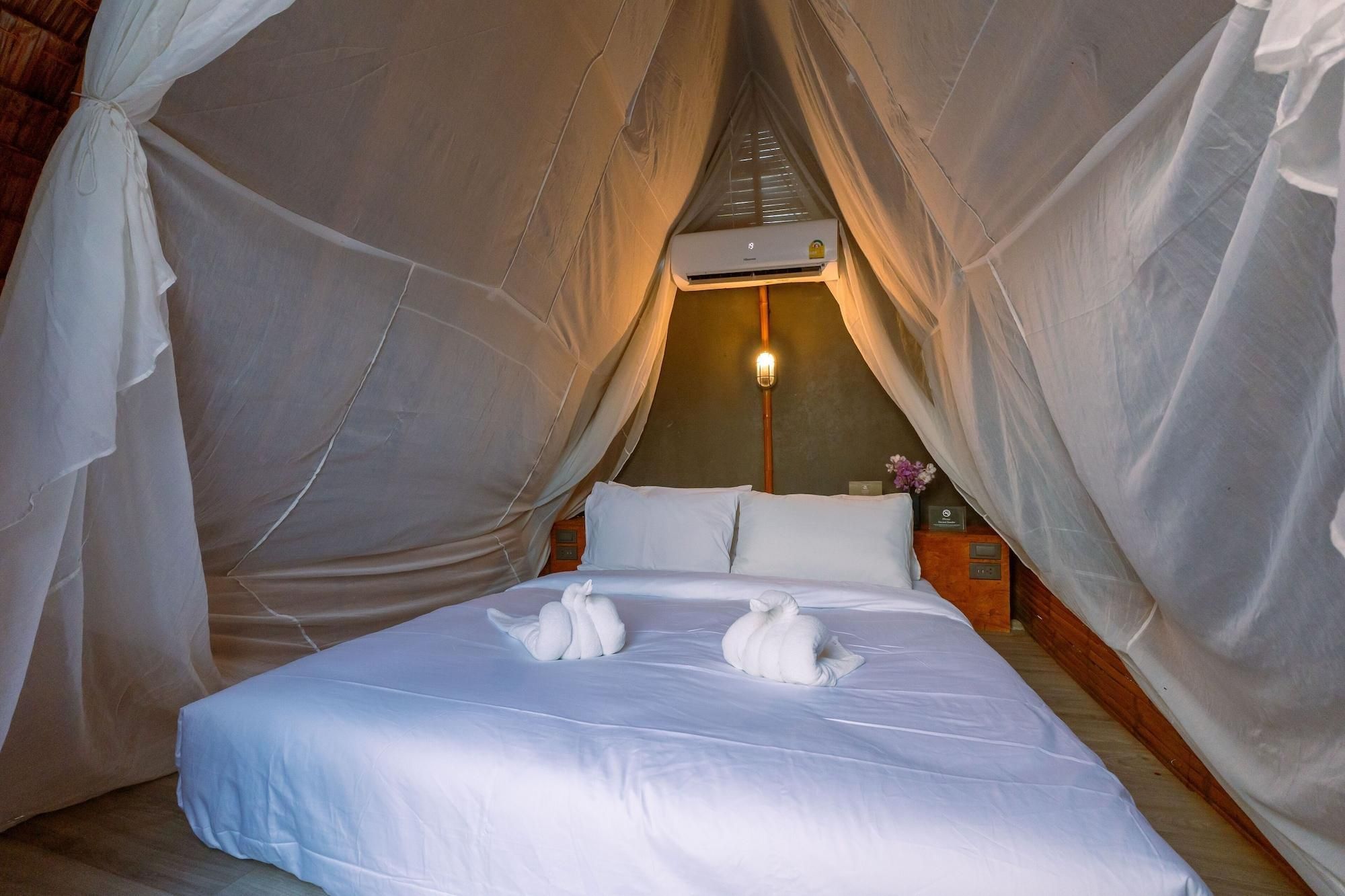 Ein Bett mit weißer Bettwäsche und zwei weißen Handtüchern, eine Wand-Klimaanlage und ein Nachttisch mit einer Lampe.