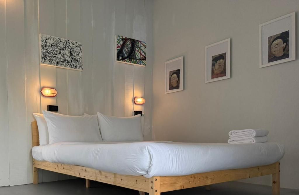 A bed with white bedding, a wooden headboard, and a wall-mounted light fixture.