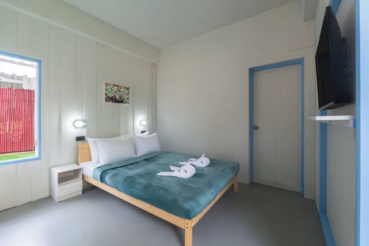 Quarto com cama, mesas de cabeceira, televisão e porta.