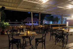 An outdoor dining area with tables and chairs, a thatched-roof structure in the background, and a covered roof overhead. - Slumber Resort Koh Chang (Ko Chang)