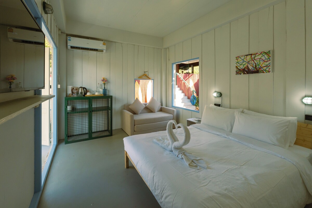 A hotel room with a bed, a desk, a chair, a window, and a wall-mounted air conditioner.