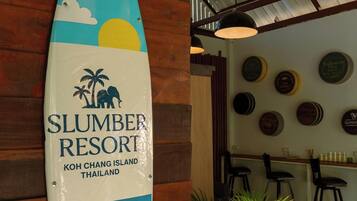 A surfboard-shaped sign for Slumber Resort in Koh Chang Island, Thailand, with a potted plant beside it.