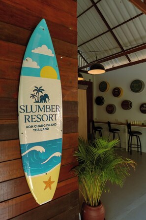 A surfboard-shaped sign for Slumber Resort in Koh Chang Island, Thailand, with a potted plant beside it. - Slumber Resort Koh Chang (Ko Chang)
