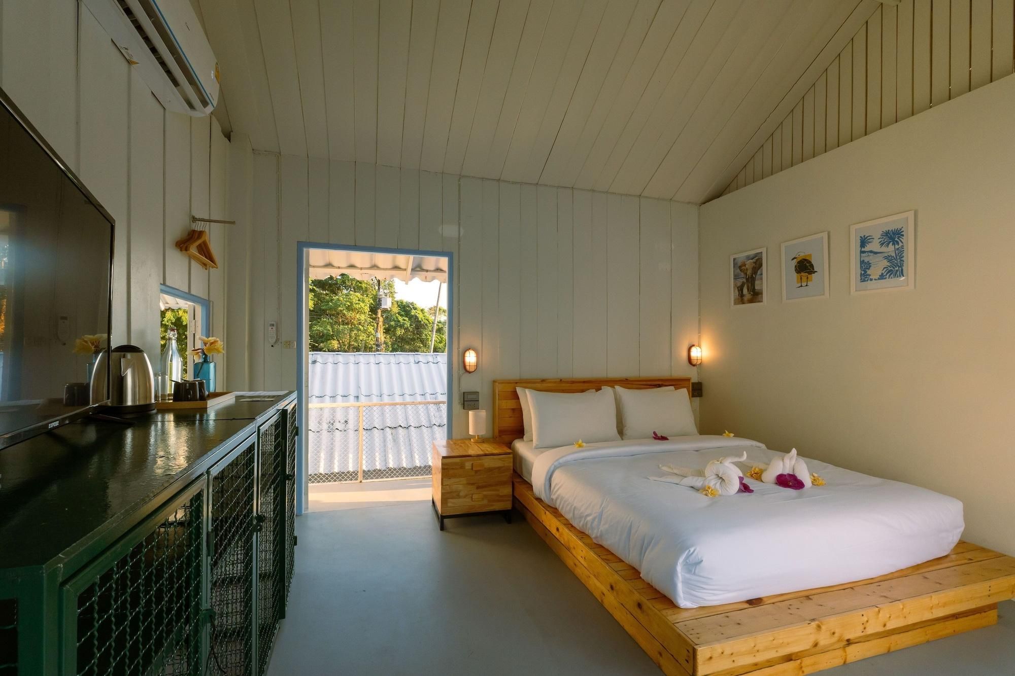 Quarto com cama, uma mesinha com chaleira, janela e porta que dá para o exterior.
