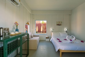 A hotel room with a bed, a desk with a coffee maker, a chair, a window with a view, and a small table with a vase of flowers. - Slumber Resort Koh Chang (Ko Chang)