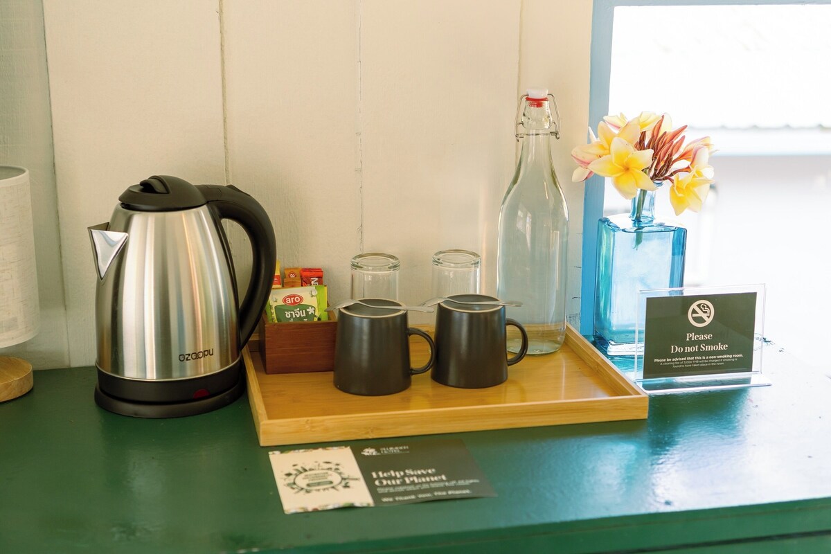 A table with a kettle, a bottle, and a tray with mugs and condiments.