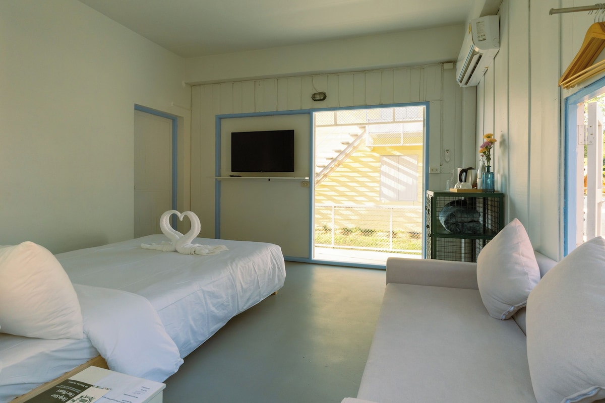 A room with two beds, a television, and a window with a view of a building.