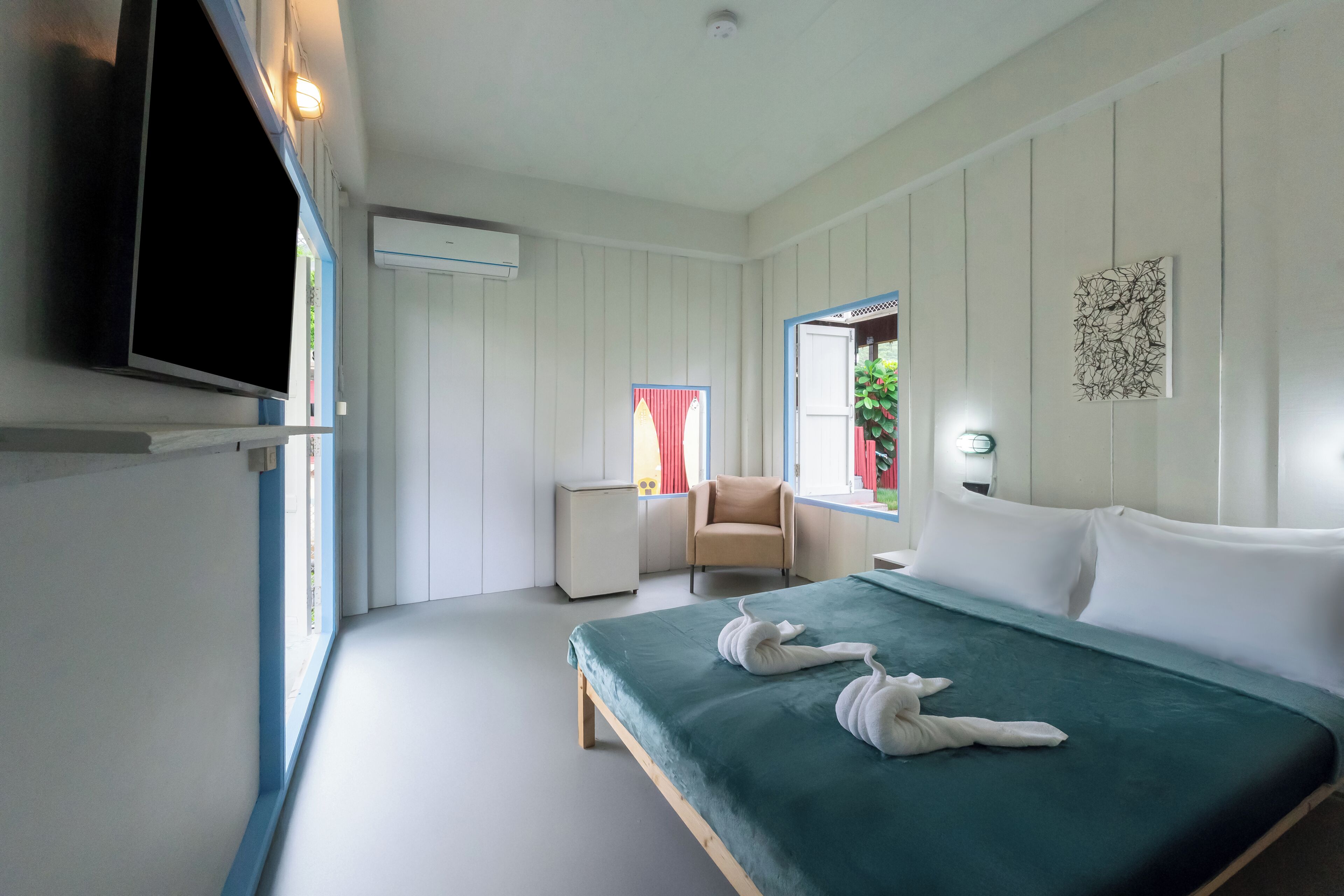 A hotel room with a bed, a TV mounted on the wall, a small bedside table, and a window with curtains.