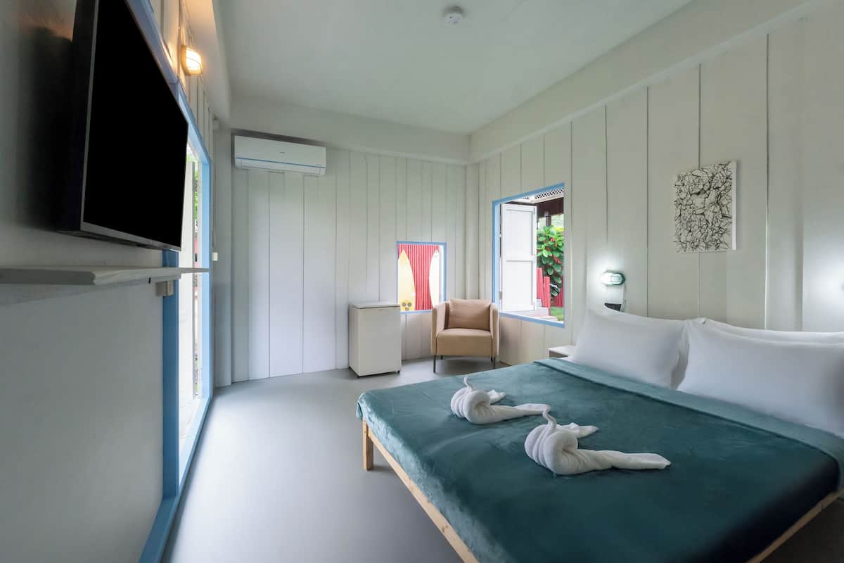 Quarto de hotel com cama, televisão presa na parede, mesa de cabeceira pequena e janela com cortinas.