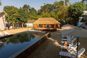 A swimming pool with lounge chairs, a thatched-roof structure, and surrounding greenery. - Slumber Resort Koh Chang (Ko Chang)
