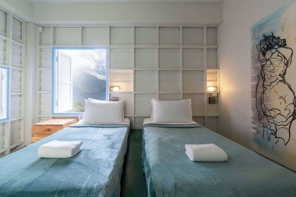 Quarto com duas camas, uma janela, um quadro e uma mesa de cabeceira de madeira.