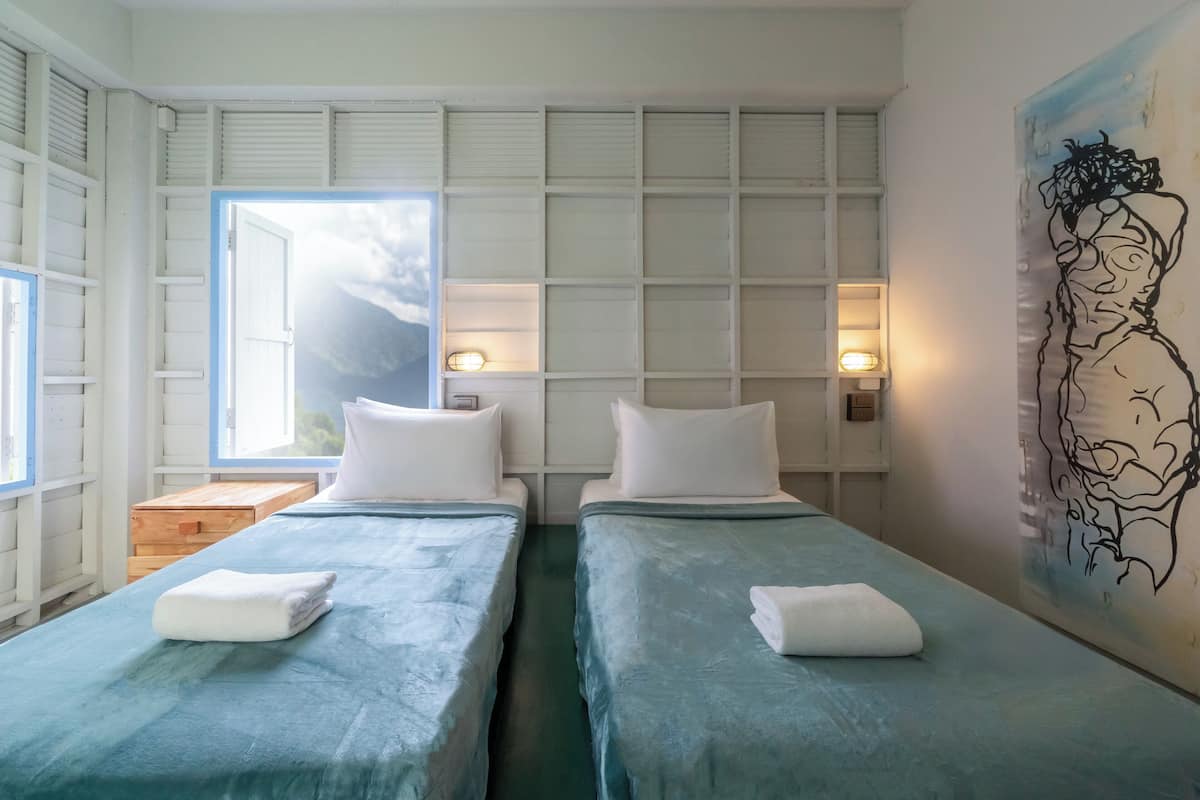 A room with two beds, a window, a painting, and a wooden nightstand.