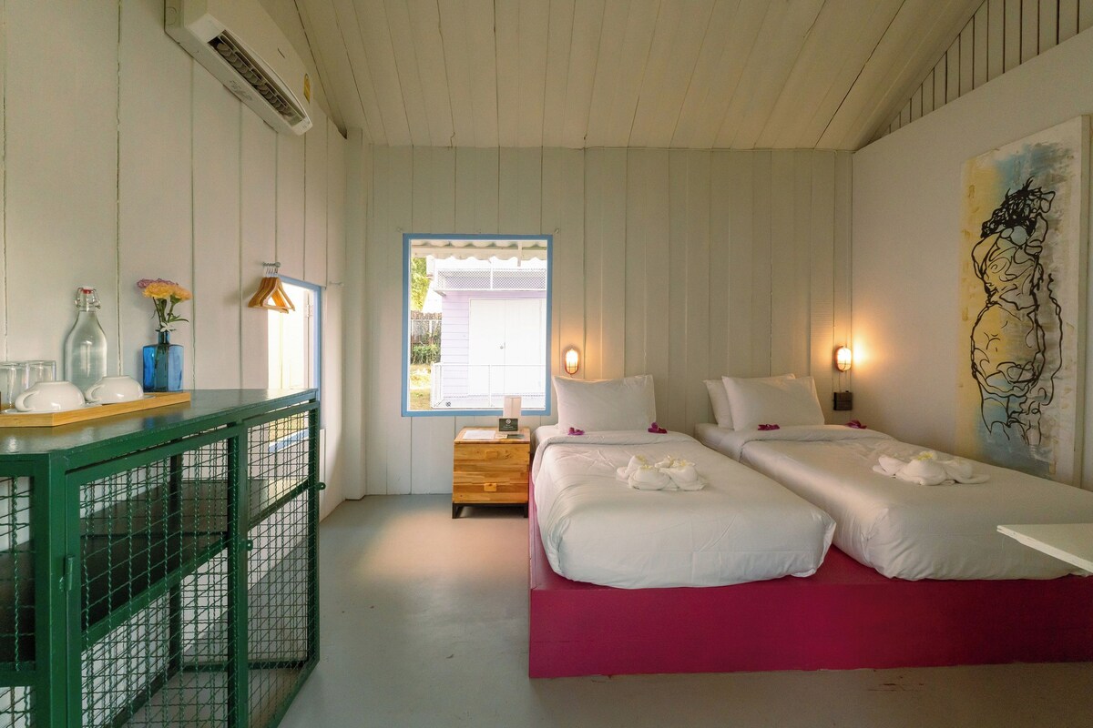 A room with two beds, a small table with a vase, and a window with a view.