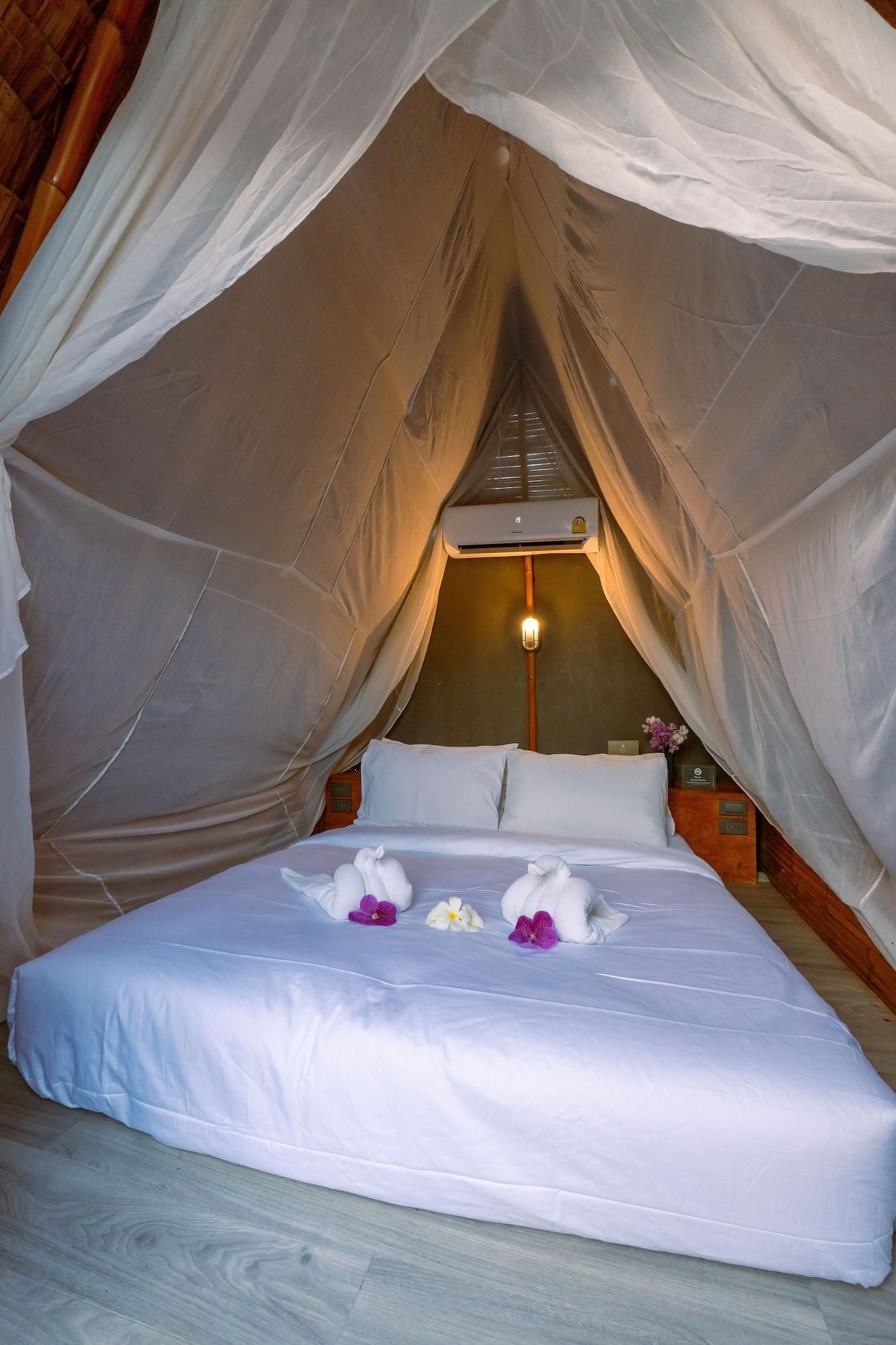 Quarto com tenda, cama, mesa de cabeceira, luminária e ar-condicionado fixado na parede.