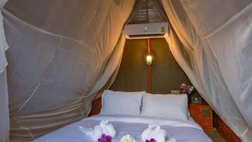 Quarto com tenda, cama, mesa de cabeceira, luminária e ar-condicionado fixado na parede.