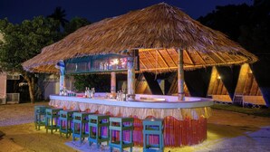 A thatched-roof bar with a counter and stools, surrounded by palm trees. - Slumber Resort Koh Chang (Ko Chang)