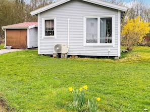A small, single-story house with a garage, a front yard with grass and daffodils, and a visible air conditioning unit.