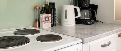 Una cocina con estufa blanca, cafetera y varias botellas sobre la encimera.
