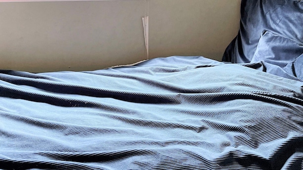 Sängyssä on raidallinen peitto, tyyny ja ikkuna, josta avautuu näkymä puihin.
