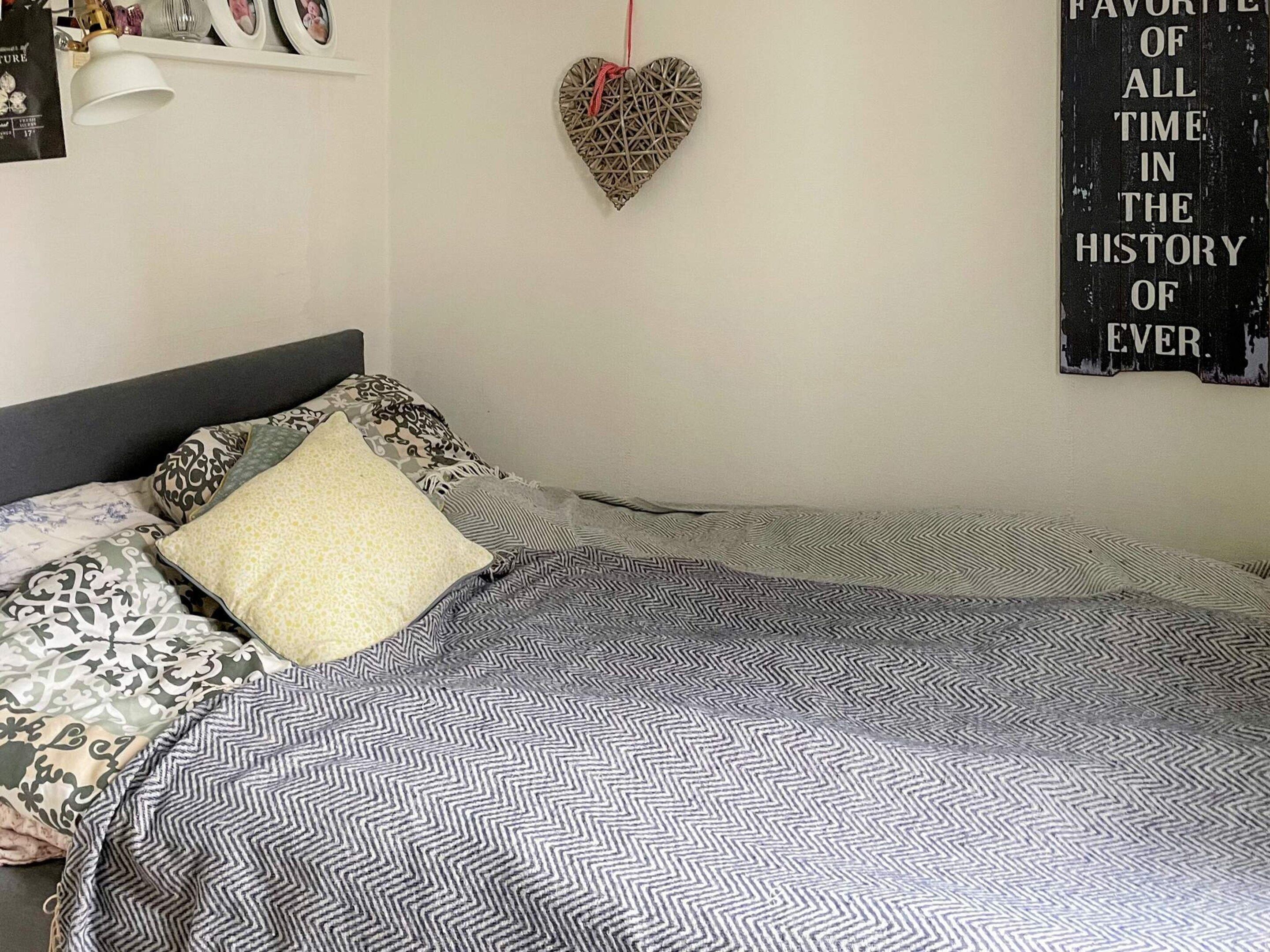 Una cama bien hecha con ropa de cama estampada, una decoración con forma de corazón en la pared y un cartel con texto.