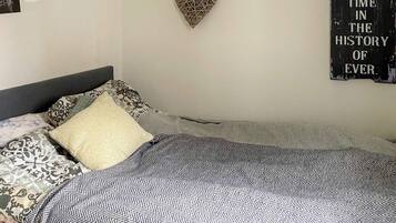 Una cama bien hecha con ropa de cama estampada, una decoración con forma de corazón en la pared y un cartel con texto.
