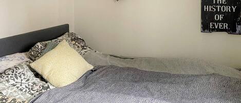 Una cama bien hecha con ropa de cama estampada, una decoración con forma de corazón en la pared y un cartel con texto.