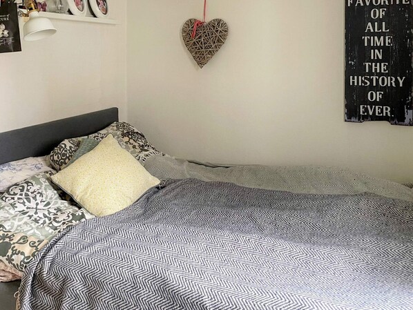 A neatly made bed with patterned bedding, a heart-shaped decoration on the wall, and a poster with text.