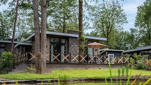 A modern building with a wooden deck and a pond in the foreground. - Modern Holiday Home With Decorative Fireplace (Hoenderloo)