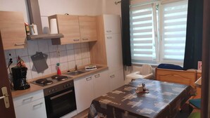 A compact kitchen with a stove, sink, and wooden cabinets. A dining table with a table runner is in the center. - Lakeside Escape With Garden Fun (Goldberg)