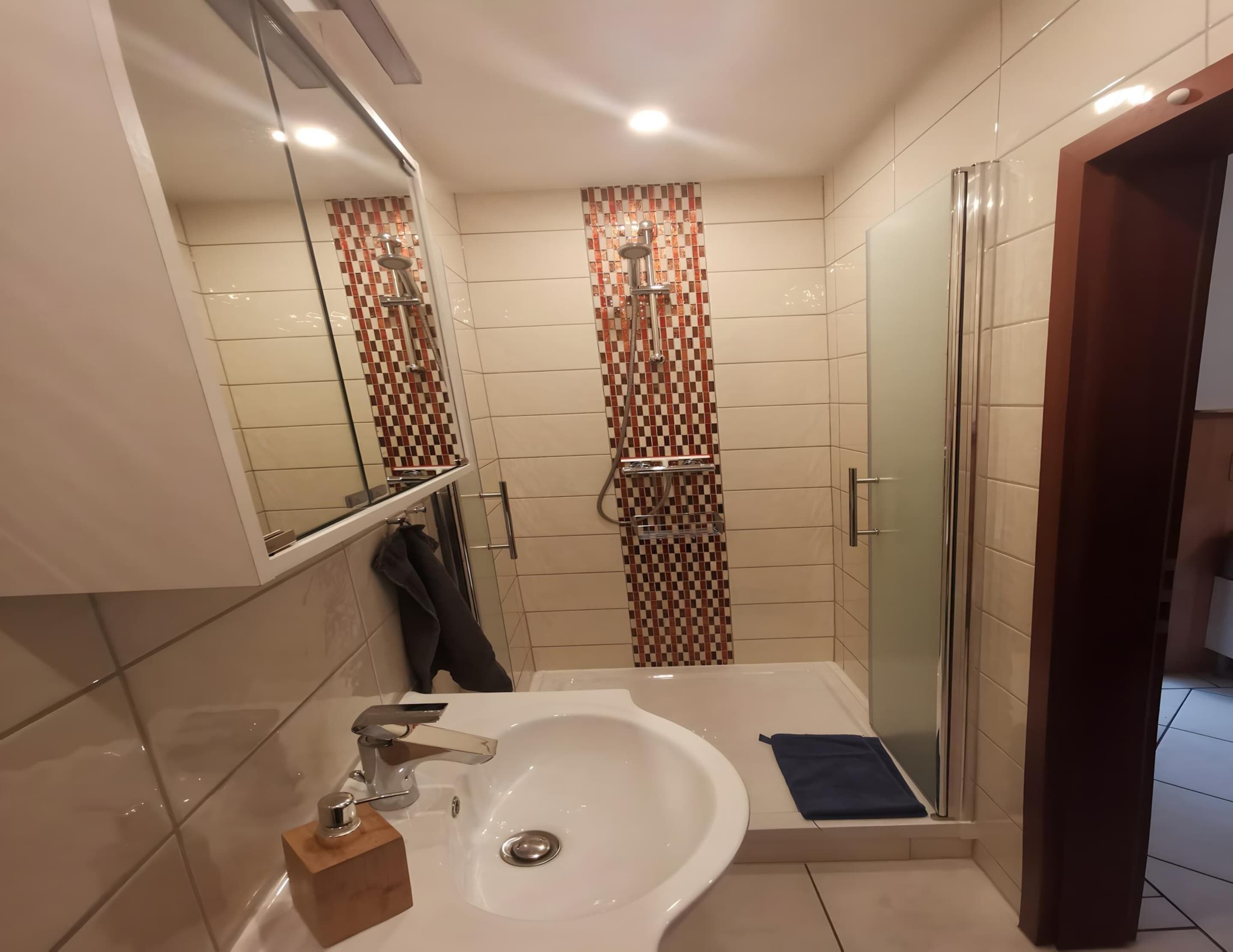 A modern bathroom with a large sink, a mirror, a shower with a checkered tile design, and a glass shower door.