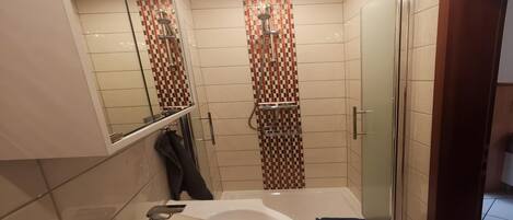 A modern bathroom with a large sink, a mirror, a shower with a checkered tile design, and a glass shower door.